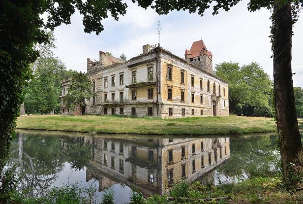 Ein verfallenes Schloss mit einem roten Turm spiegelt sich im Wasser.