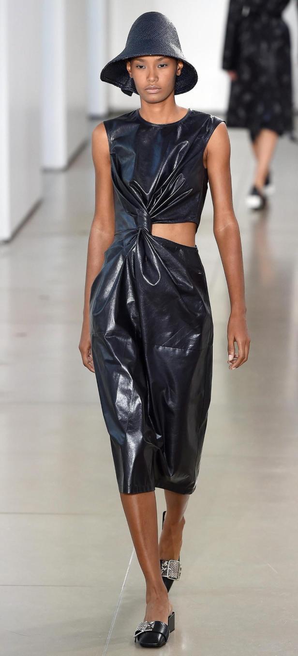 Eine Frau mit Hut und schwarzem Lederkleid läuft auf einem Laufsteg.