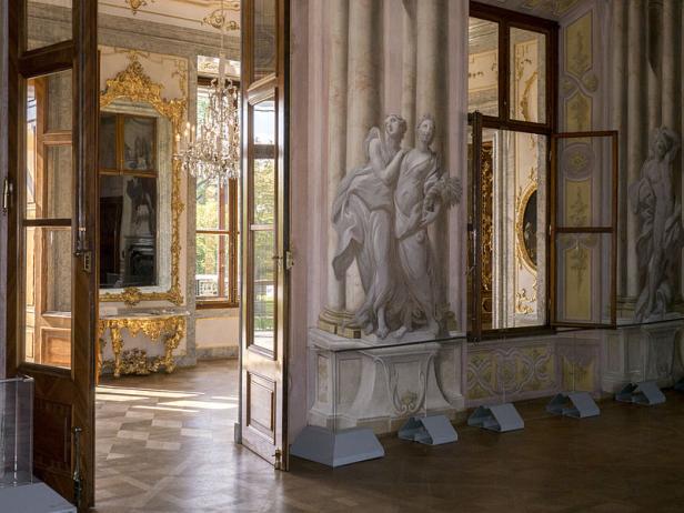 Ein prunkvoller Raum mit Wandmalereien und goldenen Verzierungen, gesehen durch eine offene Tür.