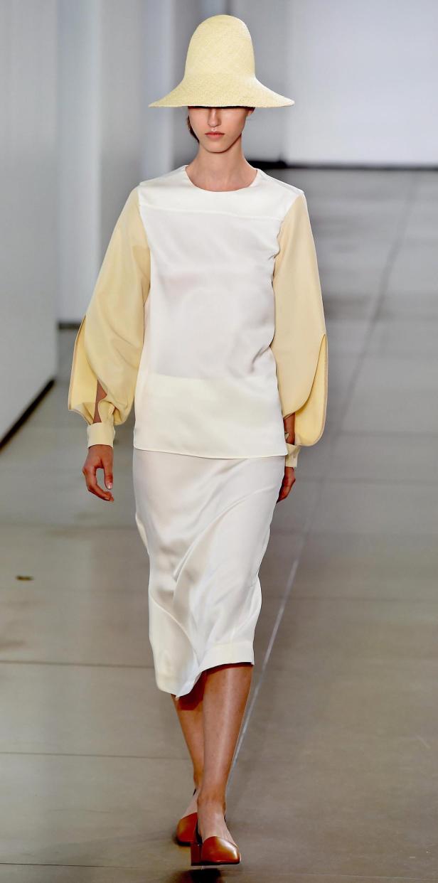 Eine Frau mit Hut und cremefarbener Kleidung läuft auf einem Laufsteg.