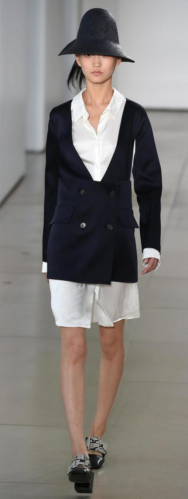 Eine Frau mit Hut trägt einen Blazer über einem weißen Hemd und Shorts.