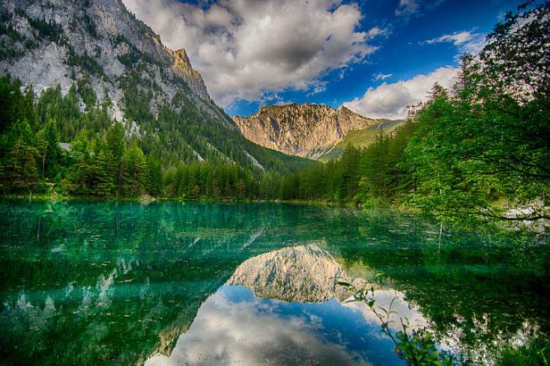 Ein Bergsee spiegelt die umliegenden Berge und den bewölkten Himmel wider.