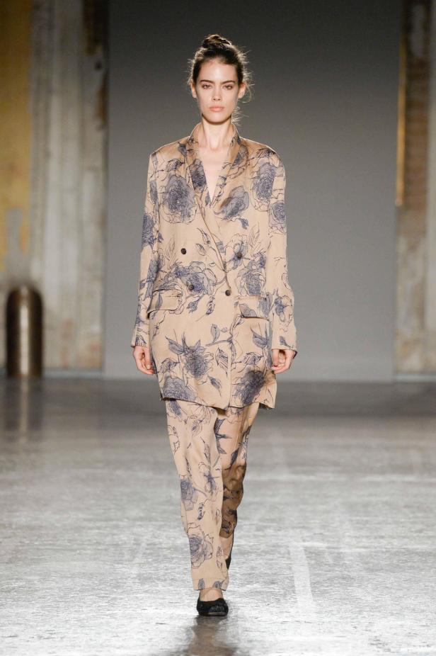 Eine Frau präsentiert einen beigen Hosenanzug mit floralem Muster.