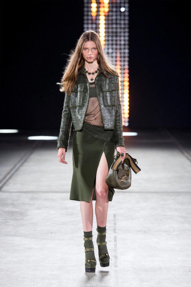 Eine Frau in einem grünen Outfit mit Jacke, Rock und Plateauschuhen auf einem Laufsteg.