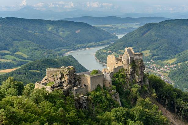 Die Burgruine Aggstein thront auf einem Felsen über der Donau, umgeben von bewaldeten Hügeln.