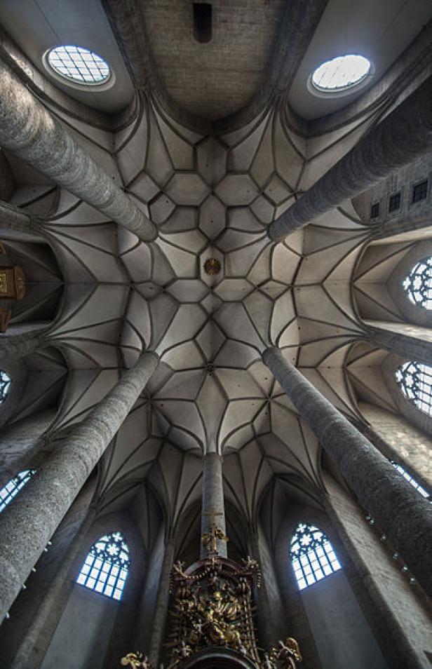 Blick auf das kunstvolle Deckengewölbe einer Kirche mit schlanken Säulen.