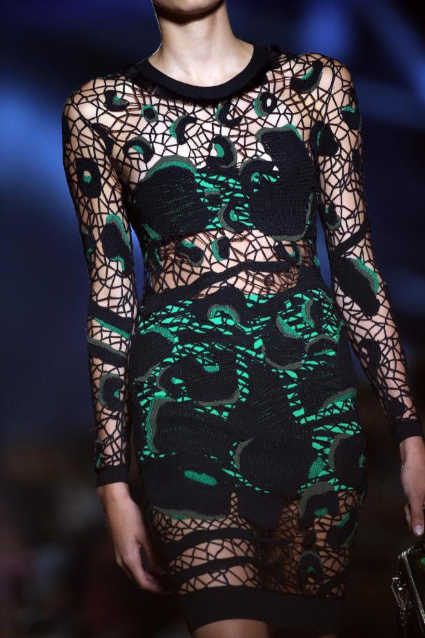 Ein Model trägt ein schwarzes, durchbrochenes Kleid mit grünen Akzenten.