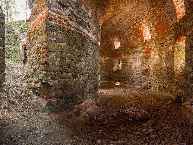 Innenansicht einer alten, verfallenen Burg mit Steinmauern und Ziegelgewölbe.