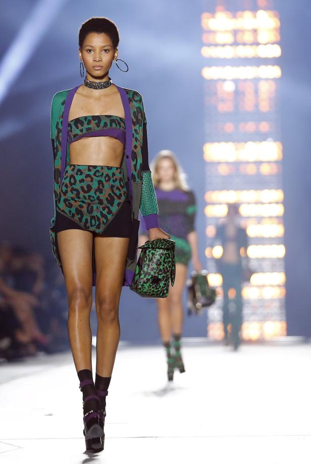 Eine Frau präsentiert ein Outfit mit Leopardenmuster und eine passende Handtasche auf dem Laufsteg.