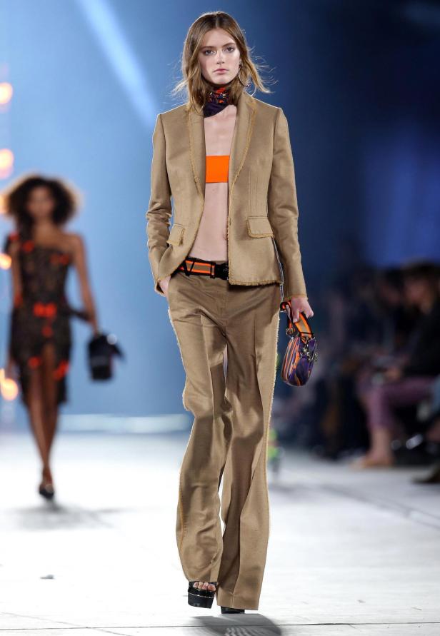 Eine Frau in einem braunen Hosenanzug und orangefarbenem Top auf einem Laufsteg.
