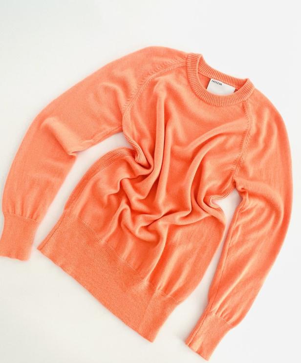 Ein orangefarbener Pullover liegt auf einem weißen Hintergrund.