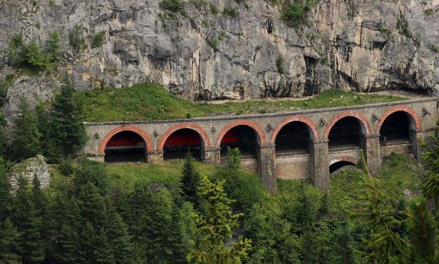 Eine alte Eisenbahnbrücke mit mehreren Tunneln vor einer Felswand.