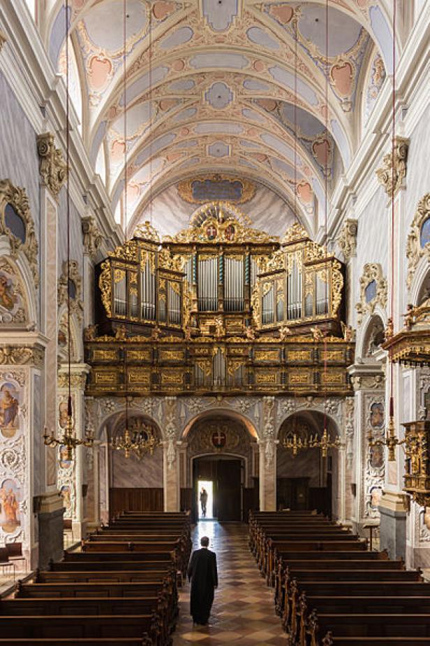 Blick in das Innere einer Kirche mit einer großen Orgel und einem Priester, der den Gang entlanggeht.