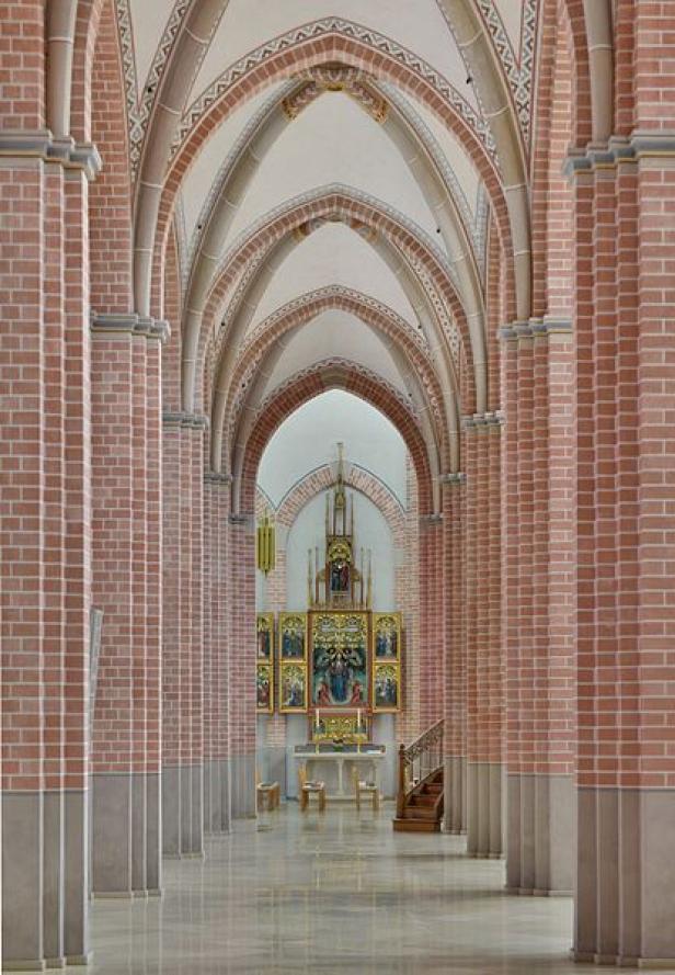 Blick durch den Gang einer Kirche mit roten Backsteinsäulen und einem Altar im Hintergrund.