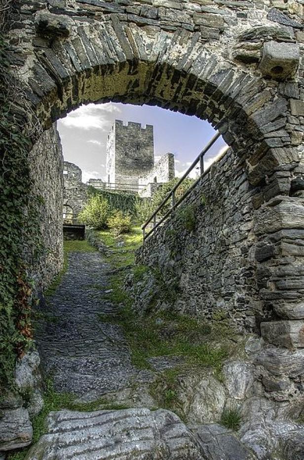 Ein Blick durch einen steinernen Torbogen auf einen Burgturm.