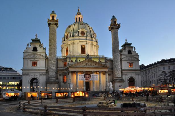 Die Karlskirche in Wien mit einem Weihnachtsmarkt im Vordergrund.