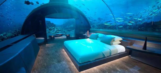 Ein Unterwasserhotelzimmer mit Blick auf ein Korallenriff und Fische.