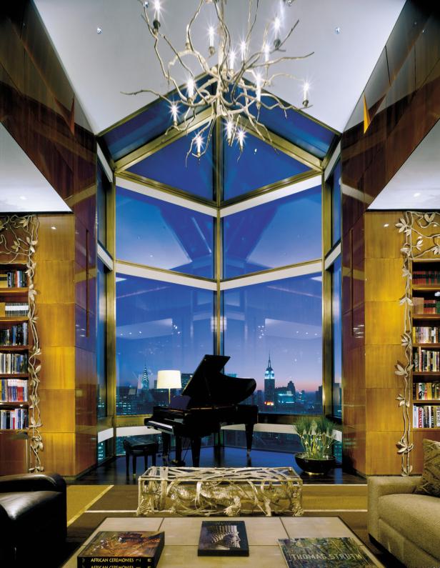 Ein luxuriöses Wohnzimmer mit Flügel, Bücherregalen und Blick auf die Skyline von New York bei Dämmerung.