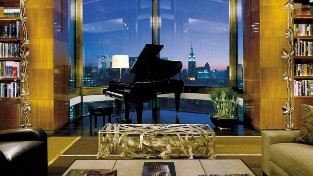 Ein luxuriöses Wohnzimmer mit einem Klavier und Blick auf die Skyline von New York bei Nacht.