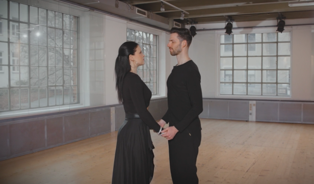 Ein Paar in schwarzer Kleidung hält Hände in einem Tanzstudio.