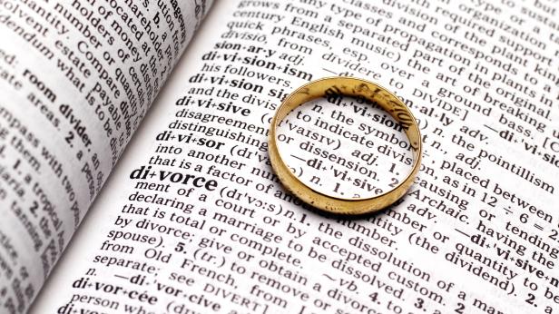 Ein goldener Ehering liegt auf einem Wörterbuch, das die Definition von „Division“ und „Divorce“ zeigt.