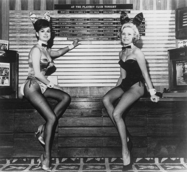 Zwei Playboy Bunnys posieren vor einer Tafel mit Namen im Playboy Club.