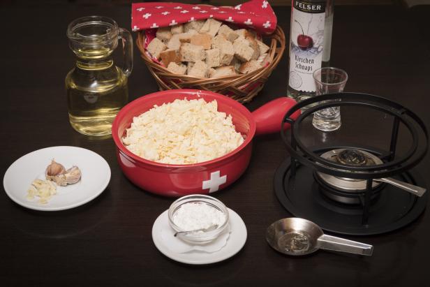 Zutaten für ein Käsefondue, darunter Käse, Brot, Knoblauch und Kirschschnaps.
