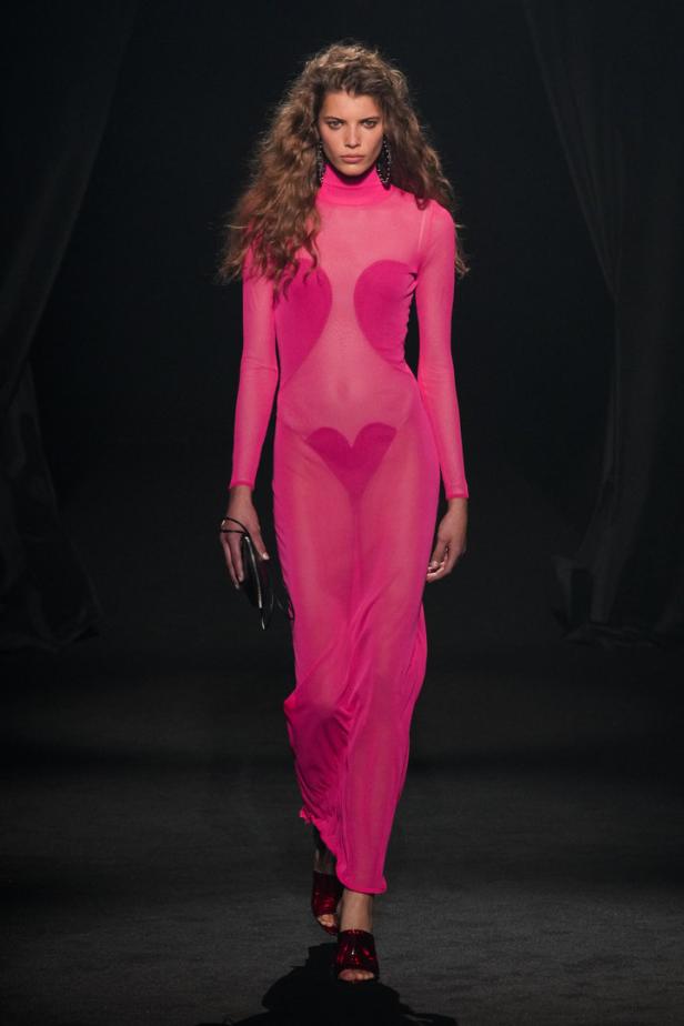 Eine Frau in einem transparenten, pinkfarbenen Kleid mit Herzapplikationen auf einem Laufsteg.