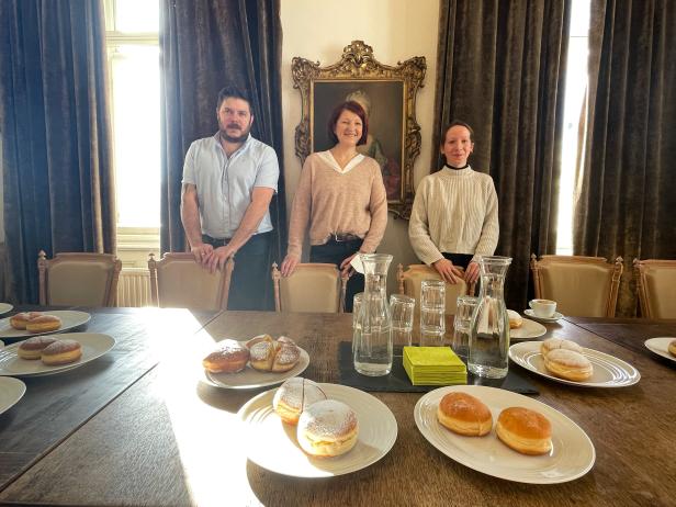 Drei Personen stehen hinter einem Tisch mit Krapfen und Getränken.