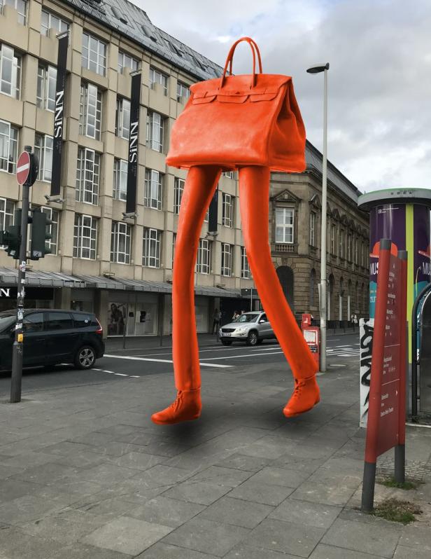 Eine orangefarbene Handtasche mit Beinen und Schuhen „läuft“ durch eine Stadt.