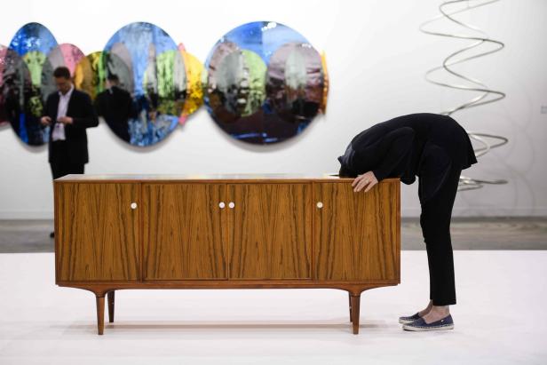 Eine Frau beugt sich über ein hölzernes Sideboard in einer Kunstgalerie.