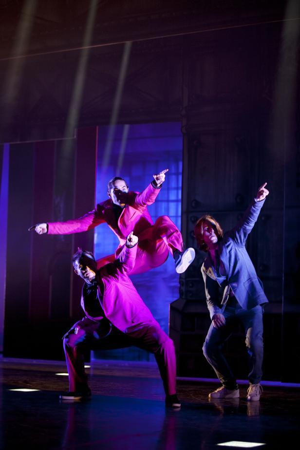 Drei Tänzer in Anzügen zeigen eine energiegeladene Performance auf der Bühne.