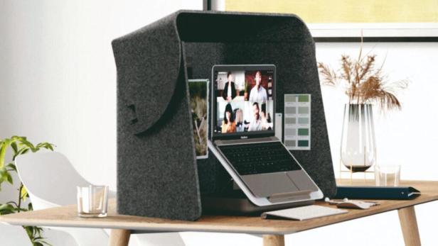 Ein Laptop steht in einer grauen, akustischen Kabine auf einem Schreibtisch für ein Online-Meeting.