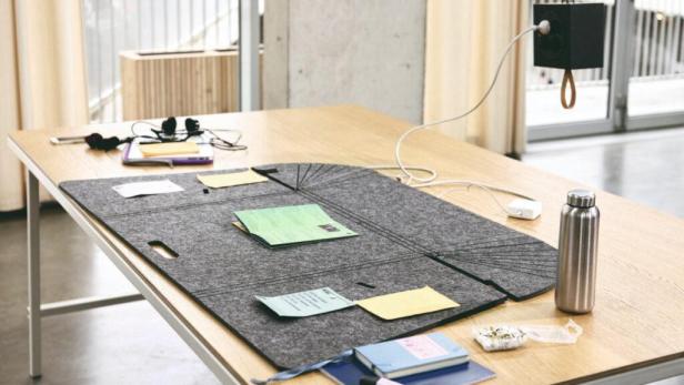 Ein Schreibtisch mit einem grauen Filz-Organizer, Notizen, einer Wasserflasche und Büroartikeln.