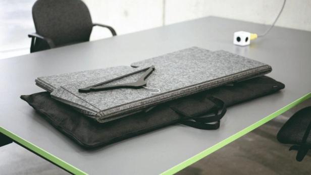 Eine graue Filzunterlage, eine schwarze Tasche und ein Kleiderbügel liegen auf einem Tisch.