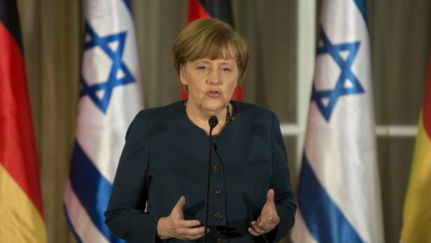 Angela Merkel spricht vor deutschen und israelischen Flaggen.