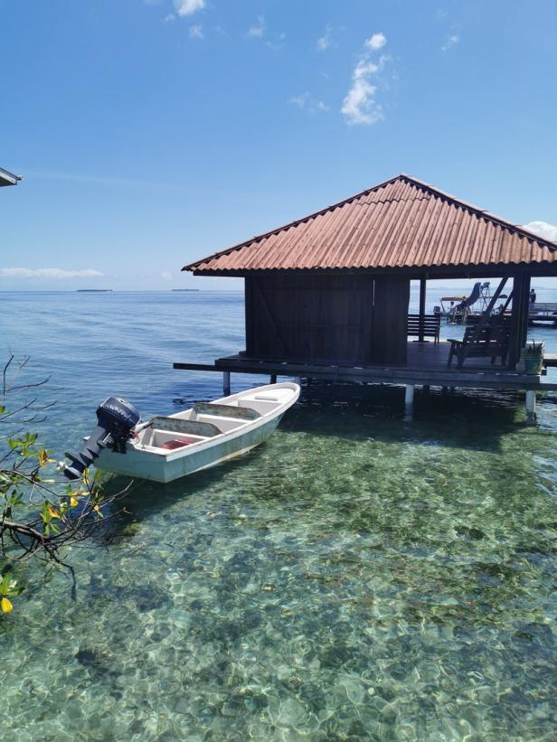 Ein Boot liegt vor einem kleinen Haus auf Stelzen im türkisfarbenen Wasser.