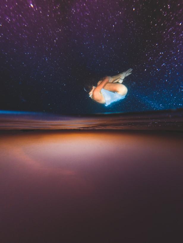 Eine Frau taucht unter Wasser, über ihr ein Sternenhimmel.