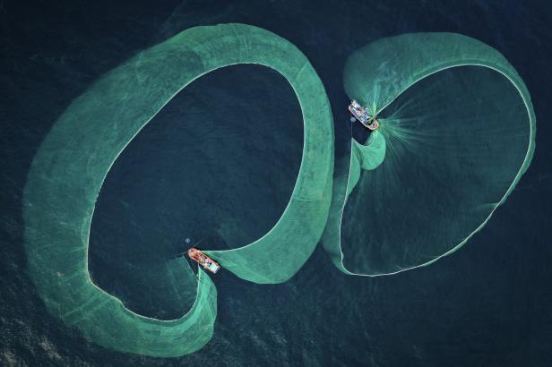 Zwei Fischerboote ziehen große Netze im Meer.