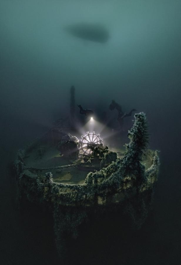 Taucher erkunden das mit Algen bewachsene Steuerrad eines versunkenen Schiffes.