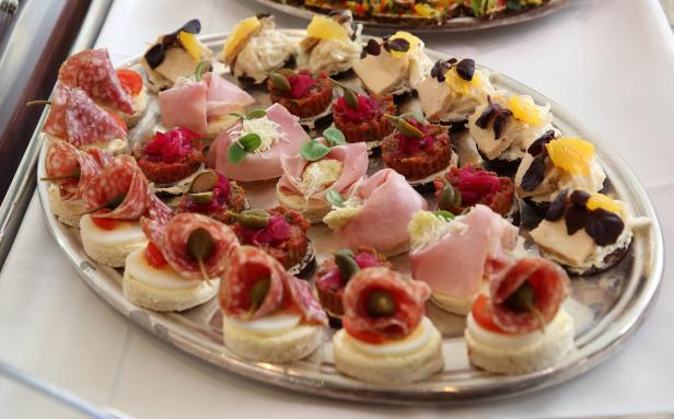 Eine Auswahl an Canapés mit Salami, Schinken, Tatar und Käse auf einem silbernen Tablett.