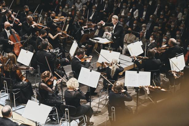 Ein Orchester spielt vor einem Publikum, viele tragen Masken.