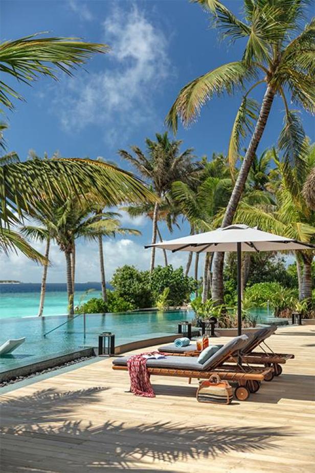 Zwei Liegestühle stehen unter einem Sonnenschirm am Pool eines tropischen Resorts.