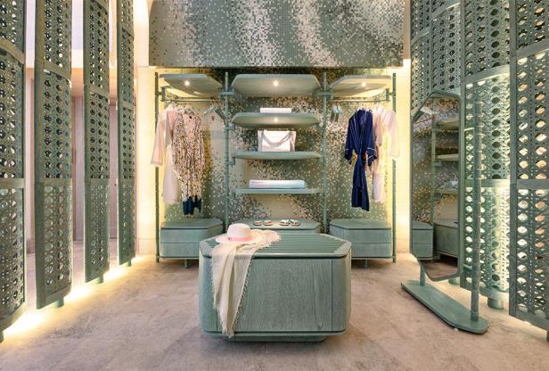 Ein begehbarer Kleiderschrank in Grüntönen mit Kleidung, Regalen und dekorativen Elementen.