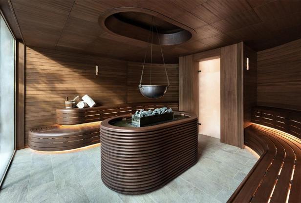 Eine moderne Sauna mit Holzbänken, einem Ofen mit Steinen und einem hängenden Wasserbehälter.