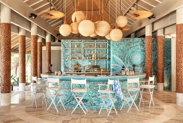 Eine Bar mit türkisfarbenen Mosaiken und weißen Barhockern in einem tropischen Resort.