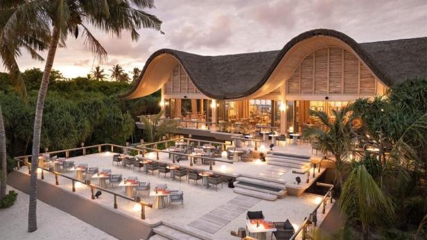 Ein Restaurant mit Strohdach und vielen Tischen im Freien bei Dämmerung.