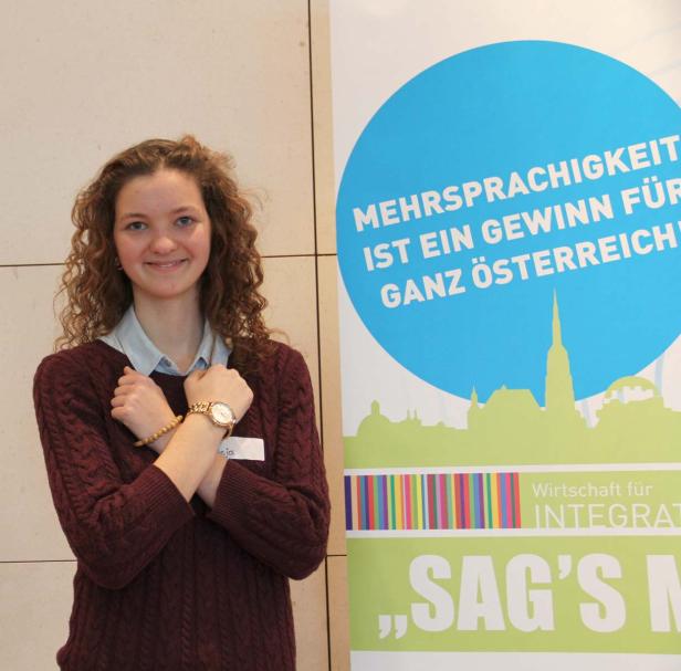 Eine junge Frau steht vor einem Banner, das Mehrsprachigkeit bewirbt.