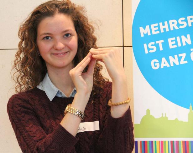 Eine junge Frau namens Anja lächelt und formt mit ihren Händen ein kleines Haus.