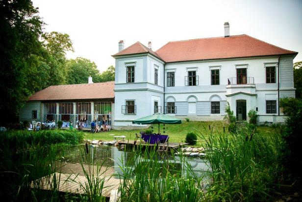 Ein weißes Gebäude mit rotem Dach steht an einem See, an dem eine Gesellschaft feiert.